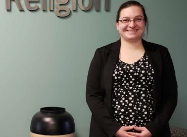 Anna Cwikla smiling in front of Department of Religion sign